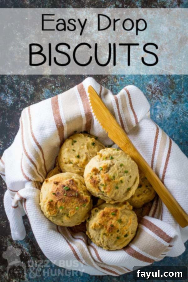 Overhead view of golden-brown drop biscuits in a bowl wrapped in a striped towel, with a wooden knife.