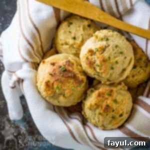 Overhead view of golden-brown drop biscuits in a bowl wrapped in a striped towel with a wooden spoon.