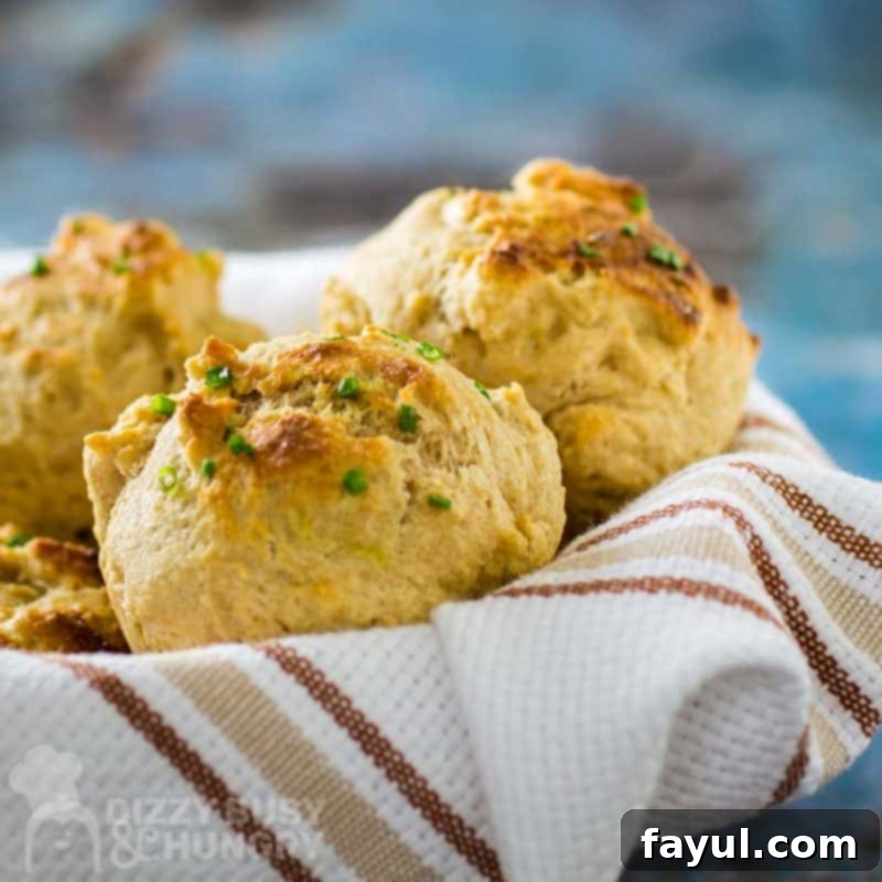 Close up shot of golden brown drop biscuits in a bowl, wrapped in a striped kitchen towel.