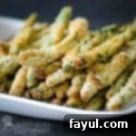 Side view of crispy baked green bean fries stacked on a white plate with a black background.