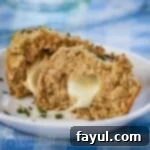 Side shot of a biscuit split in half with melted mozzarella inside, garnished with fresh herbs on a white plate.
