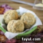 Side shot of multiple biscuits in a green bowl lined with parchment paper on a colorful cloth.