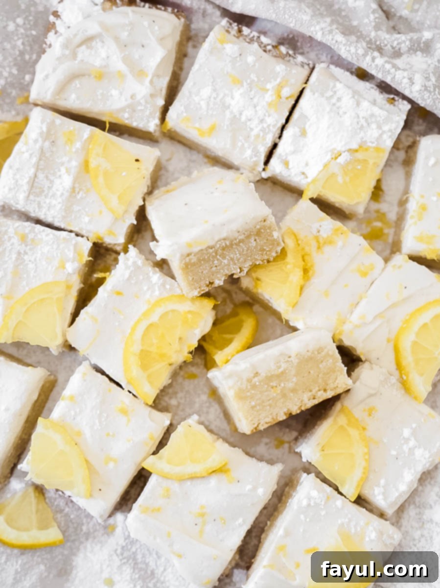 Several lemon cookie bars stacked on a plate, showing the thick frosting