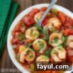 Overhead shot of shrimp stew sprinkled with herbs in a white bowl with a green cloth on the side.