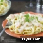 Side close up shot of shrimp fettuccine alfredo garnished with fresh parsley on an orange plate with a fork on the side.