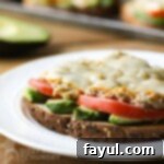 Side view of avocado tuna melt on a white plate with sliced avocado in the background.