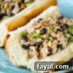 Close up side view of tuna salad sandwich garnished with herbs on a light blue plate.