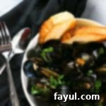 Top view of cooked mussels in a white bowl with utensils on the side