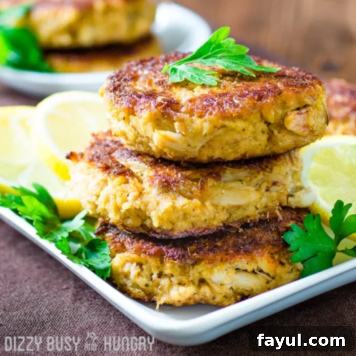 Side view of three stacked crab cakes grilled golden brown and garnished with lemon slices and parsley.