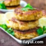 Side view of three crab cakes stacked on a white plate garnished with herbs and sliced lemons.