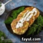 Side angled shot of three salmon patties garnished with dill sauce with a bed of dill on the side on a black plate on a blue marble surface.