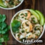 Overhead shot of shrimp in a white bowl with cilantro and lime garnish.