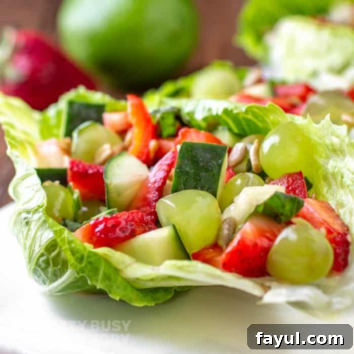 A close side view of the finished fruit and vegetable salad, beautifully presented on a crisp green lettuce leaf, resting on a white platter, highlighting its fresh textures and vibrant colors.