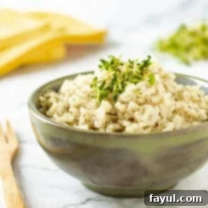 Side view of lemon dill rice garnished with herbs in an olive green bowl on a marble table with a wooden fork on the side.