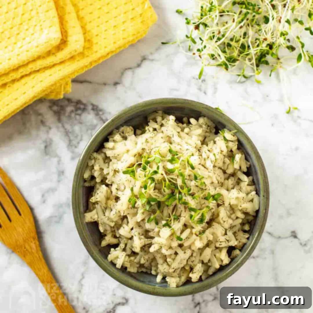 Overhead shot of lemon dill rice garnished with herbs in an olive green bowl on a marble table with a yellow cloth and wooden spoon on the side.