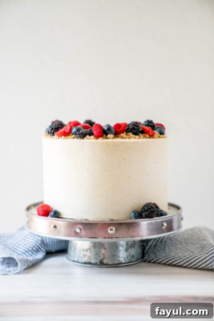 A beautifully frosted slice of Triple Berry Cake, showcasing layers of vanilla cake, berry compote, and oat crumble.