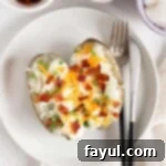 Overhead view of baked potatoes loaded with sour cream, bacon, and cheese on a white plate.
