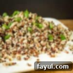 Side shot of quinoa garnished with green onions on a square white plate on a wood table.