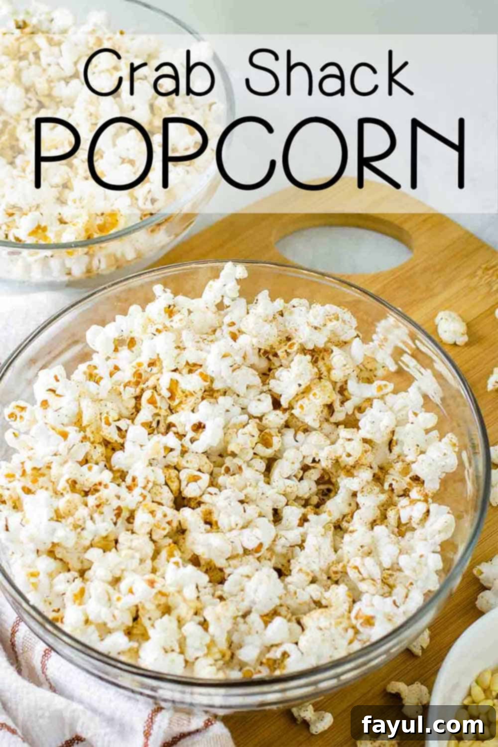 Close up shot of popcorn with homemade seasoning in a clear bowl on a wooden cutting board with popcorn sprinkled around.