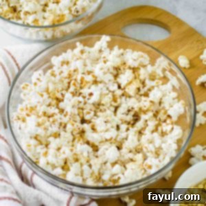 Close up shot of popcorn with homemade seasoning in a clear bowl on a wooden cutting board with popcorn sprinkled around.