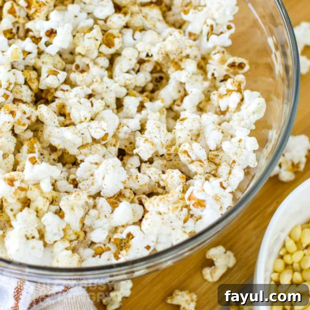 Close up overhead shot of homemade popcorn seasoning in a clear bowl on a wooden cutting board with popcorn sprinkled around.