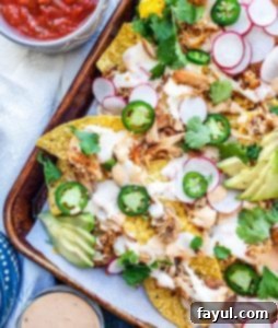 Pork Carnitas nachos on a baking tray with salsa and sauce bowls around it, ready to be served.