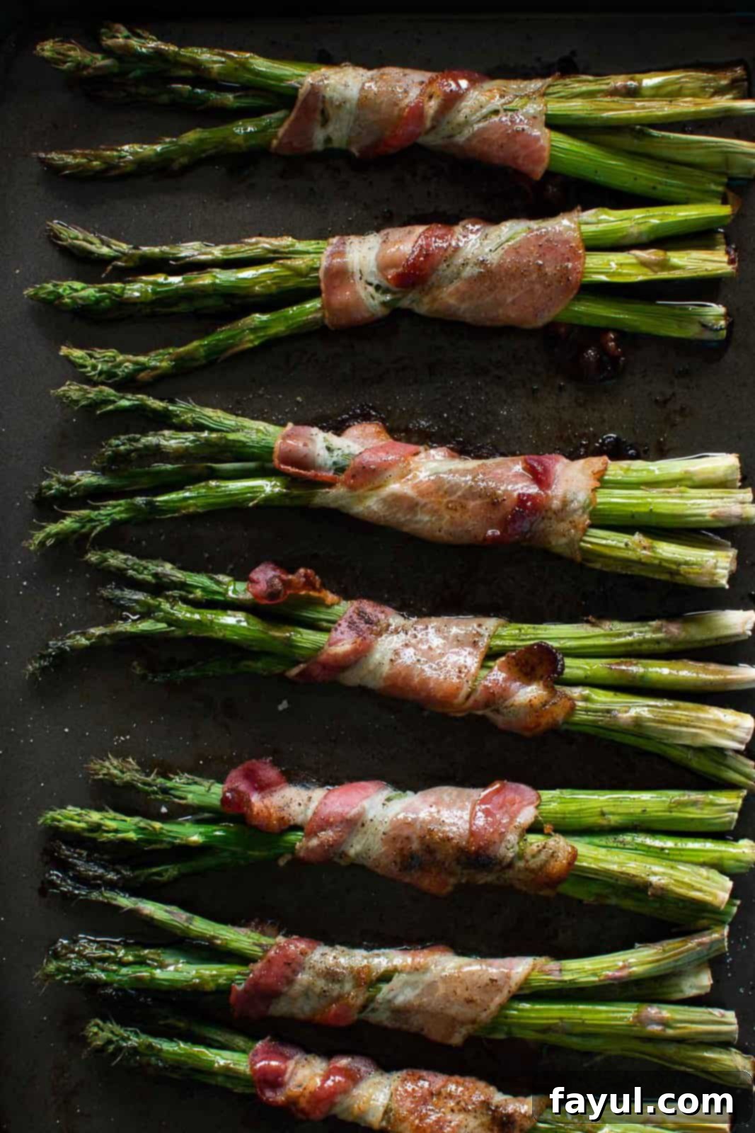 Oven baked bacon wrapped asparagus, golden brown and crispy, still on the baking sheet after cooking.