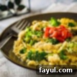Close up shot of cheesy chicken and rice on a brown plate, topped with chopped tomato.