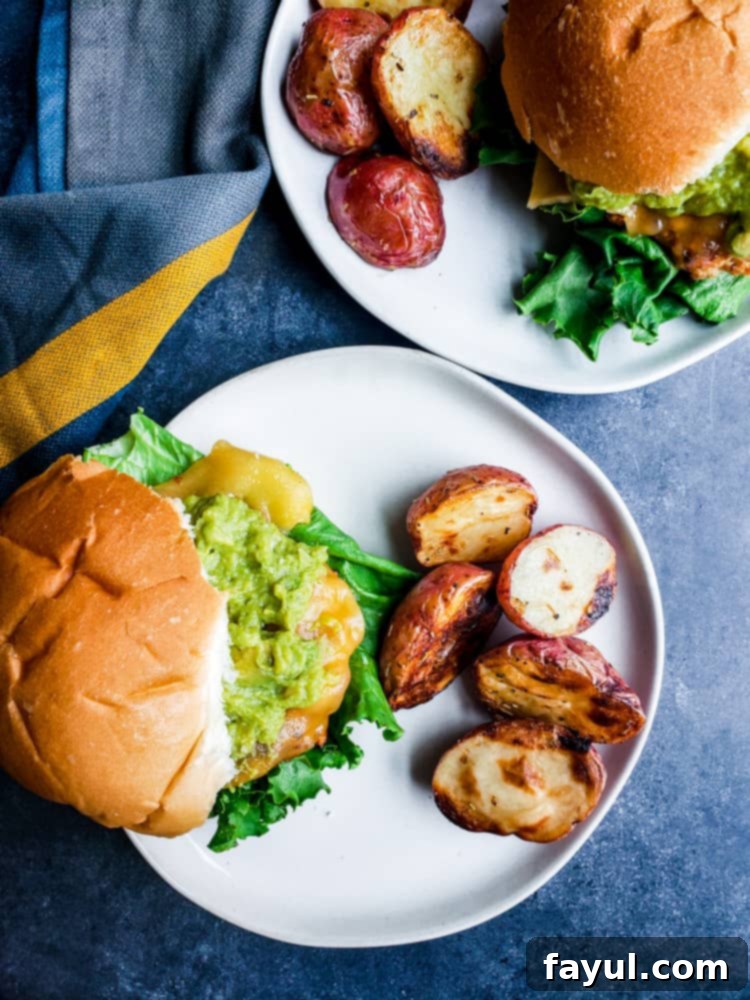 Two grilled chicken burgers on white plates, garnished with fresh toppings including guacamole and aioli. Overhead shot showcasing the finished meal.