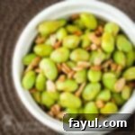 Close up overhead shot of chipotle edamame in a white bowl on a brown surface.