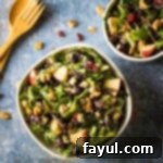 Overhead view of two apple walnut salad bowls on a black surface with a wooden spoon and fork on the side.