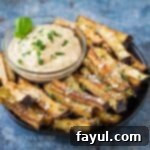 Side angle shot of crispy baked eggplant fries garnished with fresh basil and Parmesan cheese.