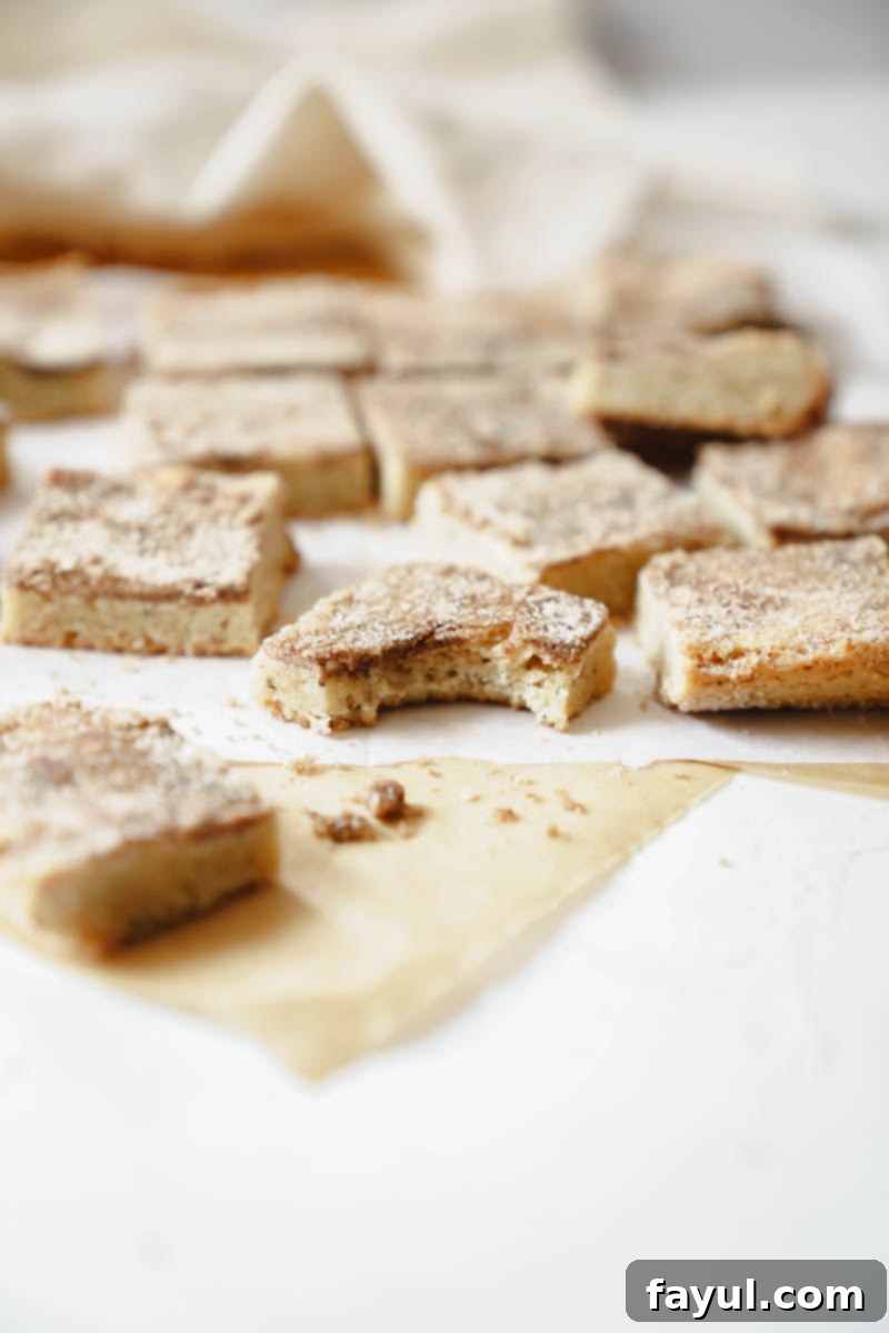 A close-up of two pieces of Brown Butter Snickerdoodle Blondies on a white surface.