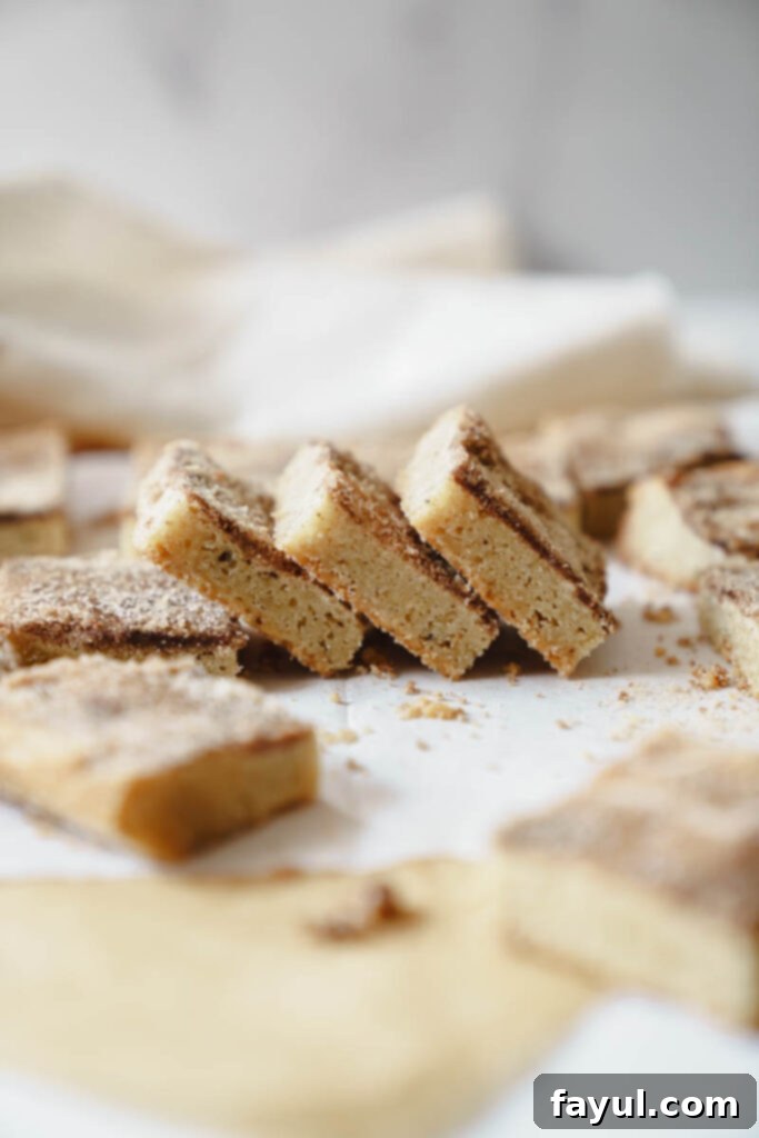 A stack of golden-brown Brown Butter Snickerdoodle Blondies, dusted with cinnamon sugar, on a white plate.