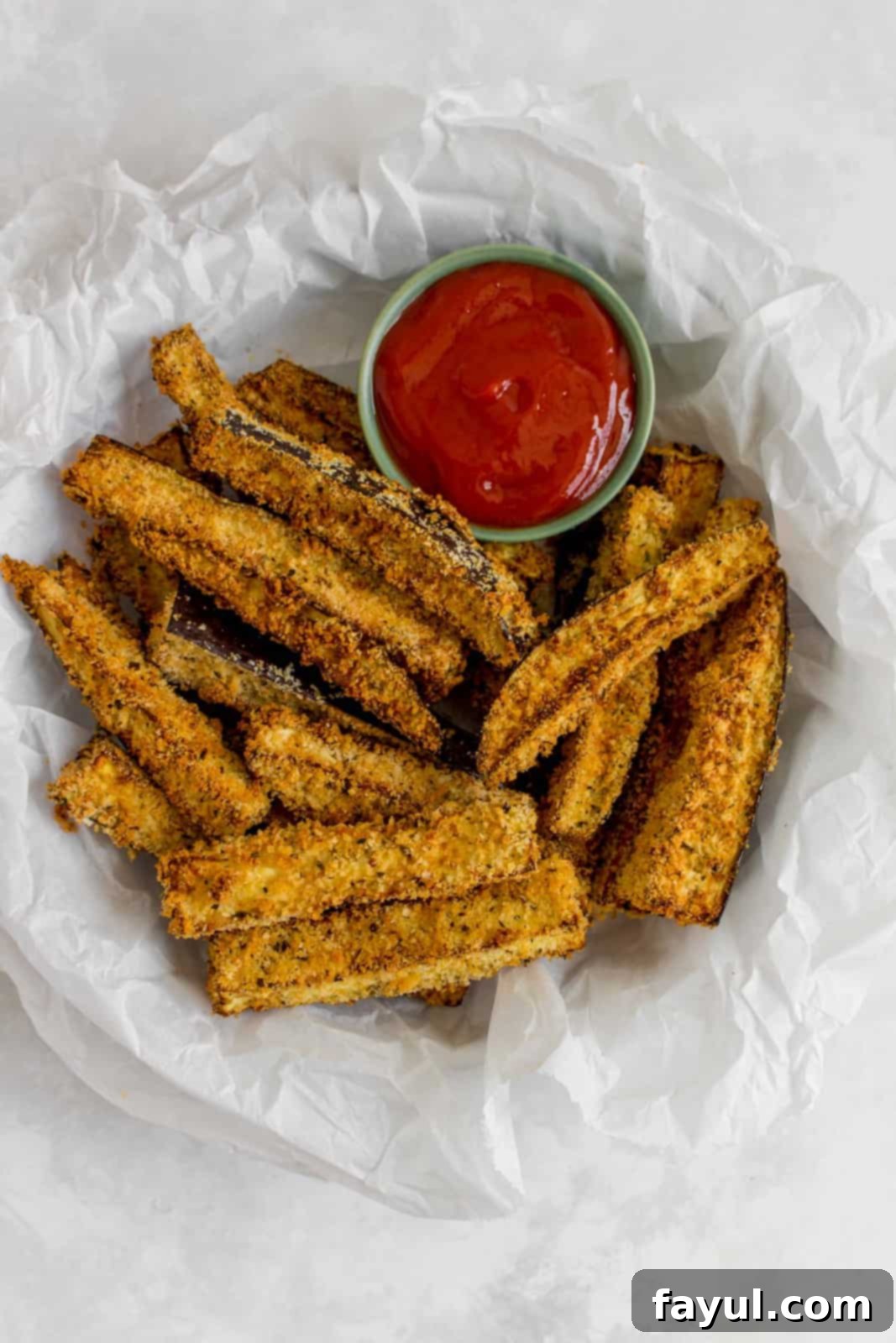 A plate with parchment paper, containing air fryer eggplant fries and dip.