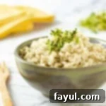 Side view of lemon dill rice garnished with herbs in an olive green bowl on a marble table with a wooden fork on the side.