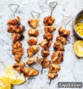 Overhead shot of chicken on four skewers on a white marble counter with lemons on the side. 