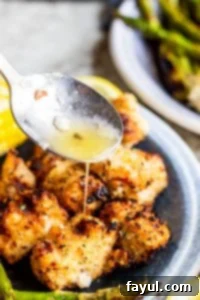 Silver spoon pouring lemon butter sauce over chicken on a blue plate.