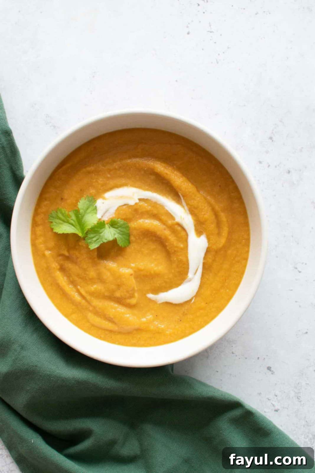 A beautifully presented bowl of homemade carrot lentil soup, garnished, with a green tablecloth on the side, inviting you to enjoy this comforting meal.