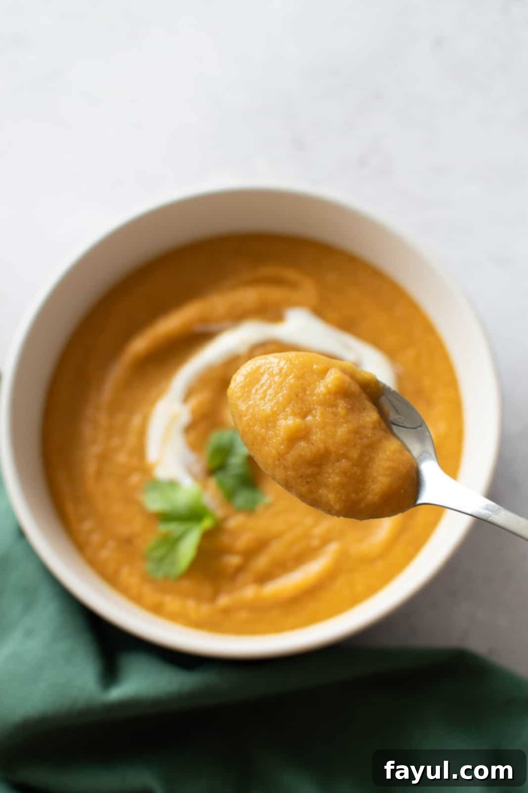 A spoon filled with creamy carrot lentil soup is held above a bowl of the delicious soup, inviting a taste. It's the perfect healthy dinner for cold fall and winter nights!