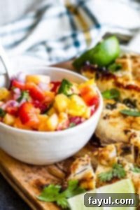 Close-up of fresh Strawberry Pineapple Salsa in a white bowl, with a hint of grilled chicken in the background, showcasing a perfect pairing.