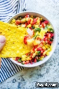 Tortilla chip being held with salsa on it and white bowl blurred underneath. 