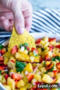 Hand reaching into strawberry pineapple salsa with a tortilla chip.