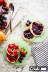Overhead shot of jam on bagels on green plates on a white counter.