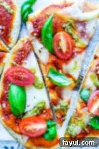 The best, easy homemade Margherita Naan Pizza Recipe! The recipe uses naan bread, tomatoes, mozzarella cheese, fresh basil, and basil pesto and is ready in under 15 minutes making it the perfect weeknight dinner recipe for families. Bonus is this recipe is freezer friendly and makes great leftovers. Simple step by step instructions and VIDEO! #pizza #recipe #easyrecipes #dinner #margheritapizza #weeknightdinner Naan pizza sliced on a cutting board.
