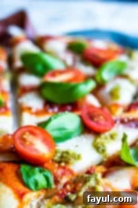 The best, easy homemade Margherita Naan Pizza Recipe! The recipe uses naan bread, tomatoes, mozzarella cheese, fresh basil, and basil pesto and is ready in under 15 minutes making it the perfect weeknight dinner recipe for families. Bonus is this recipe is freezer friendly and makes great leftovers. Simple step by step instructions and VIDEO! #pizza #recipe #easyrecipes #dinner #margheritapizza #weeknightdinner Close up of margherita pizza covered in tomatoes and basil.