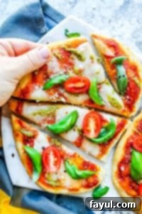 The best, easy, homemade Margherita Naan Pizza Recipe! The recipe uses naan bread, tomatoes, mozzarella cheese, fresh basil, and basil pesto and is ready in under 15 minutes making it the perfect weeknight dinner recipe for families. Bonus is this recipe is freezer friendly and makes great leftovers. Simple step by step instructions and VIDEO! #pizza #recipe #dinner #margheritapizza #easyrecipe Hand picking up a slice from the margherita pizza recipe. Pizza is on a marble cutting board and white counter.