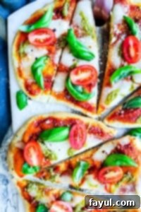 The best, easy homemade Margherita Naan Pizza Recipe! The recipe uses naan bread, tomatoes, mozzarella cheese, fresh basil, and basil pesto and is ready in under 15 minutes making it the perfect weeknight dinner recipe for families. Bonus is this recipe is freezer friendly and makes great leftovers. Simple step by step instructions and VIDEO! #pizza #recipe #easyrecipes #dinner #margheritapizza #weeknightdinner Two pizzas on a cutting board on a white counter top.