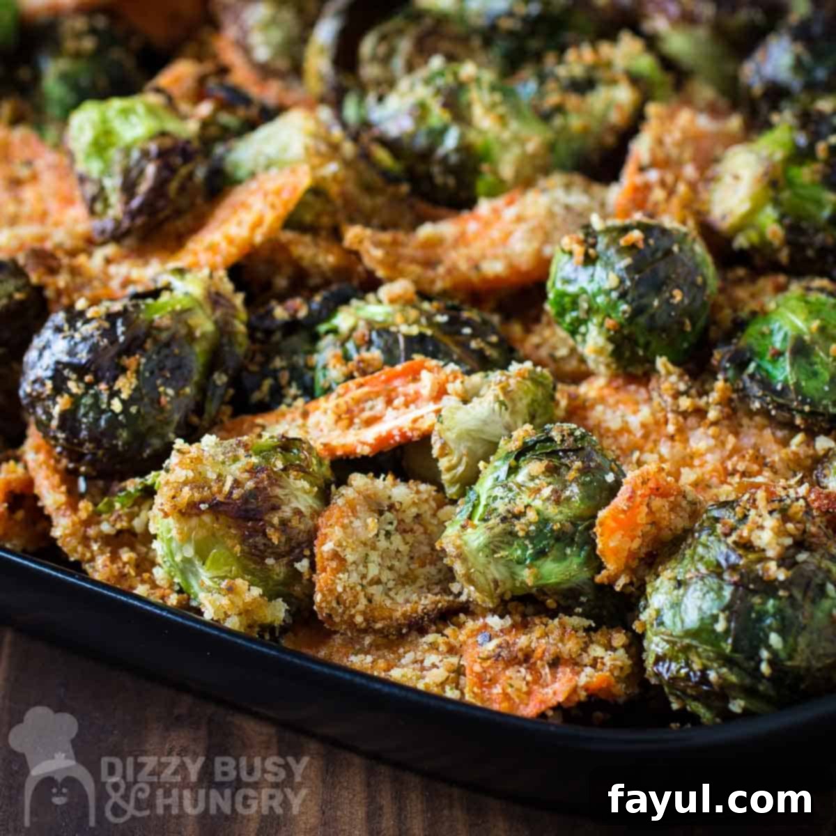 Side close up shot of roasted Brussel sprouts and carrots on a black plate on a dark wooden surface.