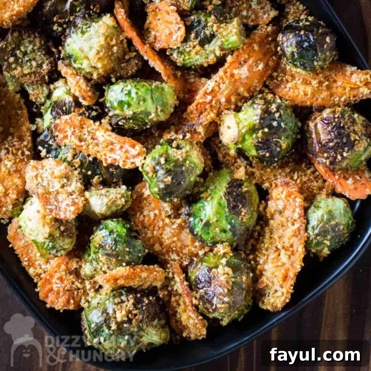 Close up overhead shot of roasted Brussel sprouts and carrots on a black plate on a dark wooden surface.
